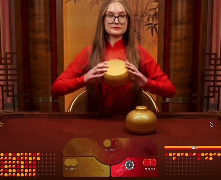 A dragon dragon live dealer shaking a gold bowl above the betting panel showing 0.95:1 on the mixed spot and 2.90:1 on each colour