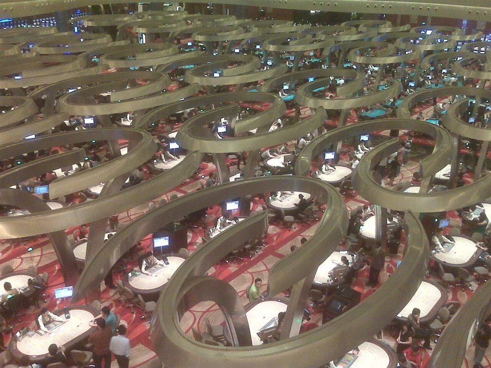 How to play baccarat shown across a casino baccarat pit with road displays at each table