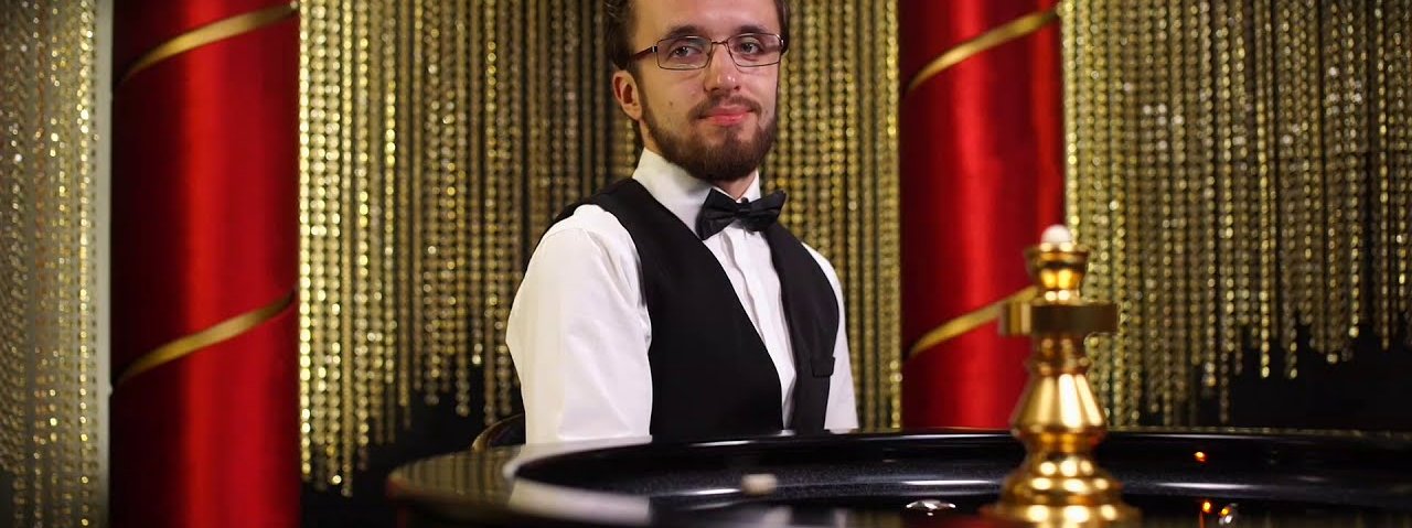 Speed Roulette live dealer in a waistcoat and bow tie behind the wheel in the red and gold studio