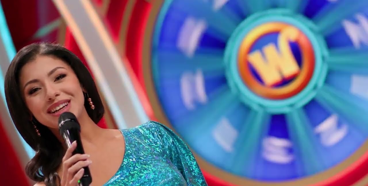 The Bingo Spot host with a microphone in front of the blue Wild Ball bonus wheel