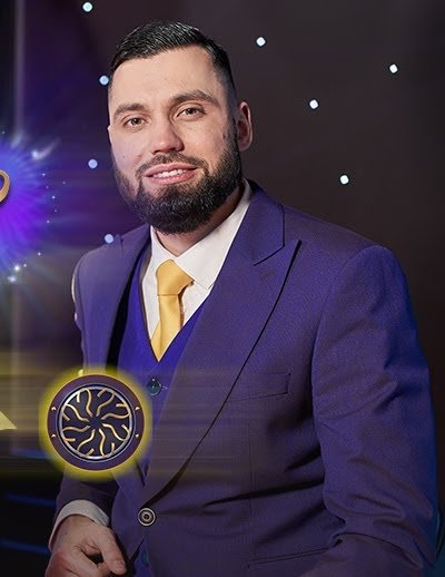 Who Wants To Be A Millionaire Live Roulette host in a purple suit beside a question-mark icon and a Millionaire coin