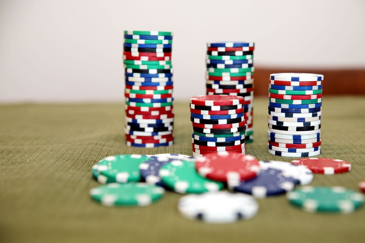 Three tall stacks of red, green, blue, black and white casino chips on felt with loose chips in front