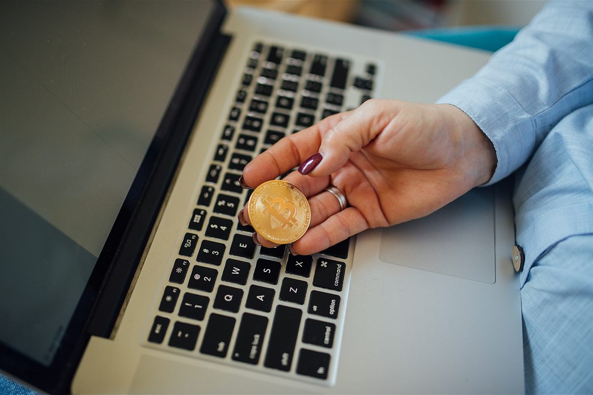 Hand holding a Bitcoin over a laptop before a crypto deposit